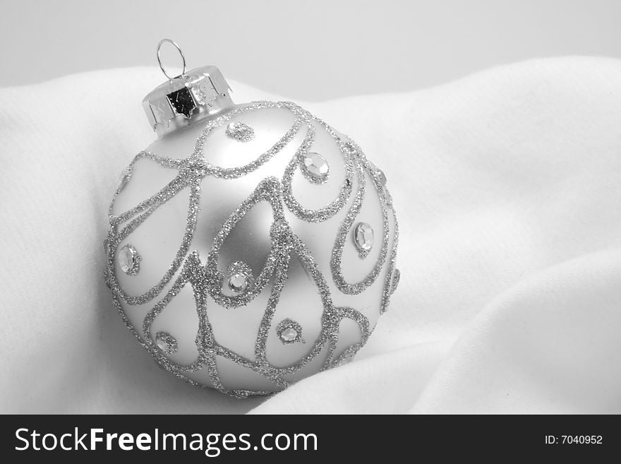 Silver, glittery ornament against soft, white cotton fabric. Silver, glittery ornament against soft, white cotton fabric