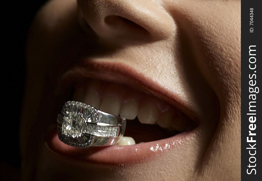 Close up shot of sensual lips holding a diamond ring. Close up shot of sensual lips holding a diamond ring