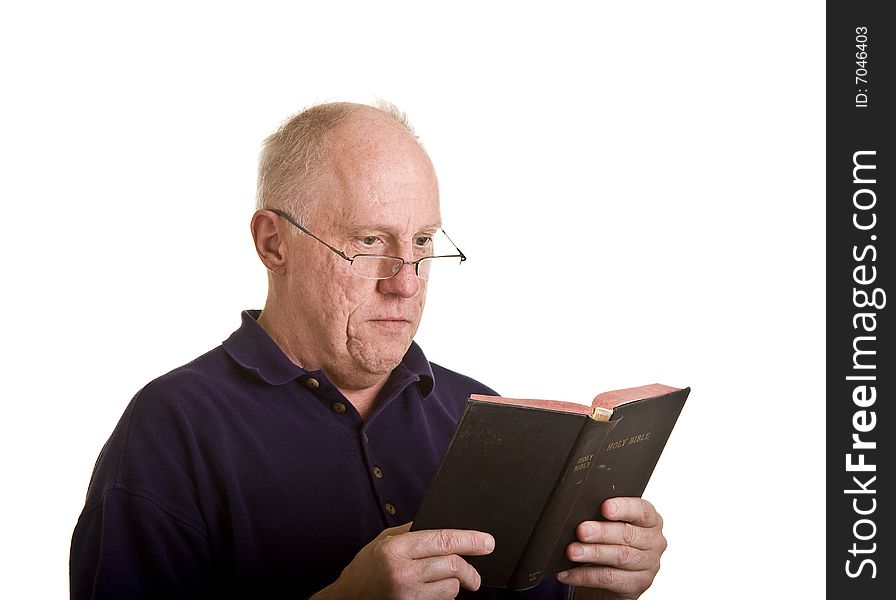 An older bald man in glasses reading the bible with interest. An older bald man in glasses reading the bible with interest