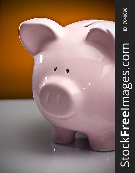 Ceramic pink piggy bank on white surface with orange spotlight background. Savings concept.