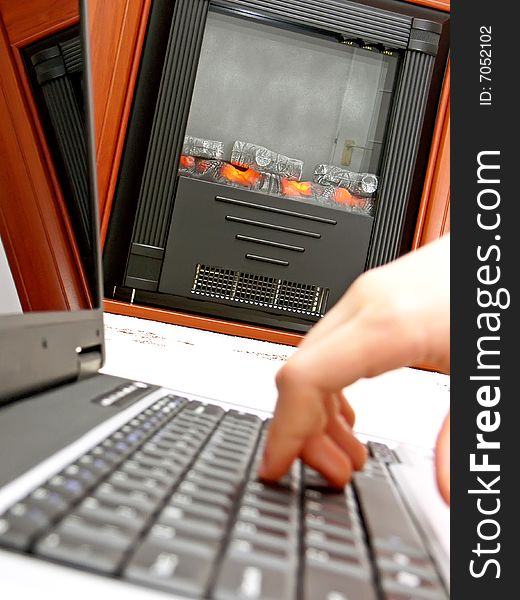 Close up of hand on the laptop keyboard and the fireplace in the background.