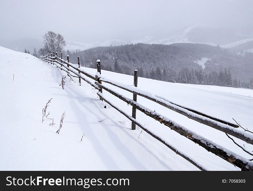 Snowy field and fence in winter mountains