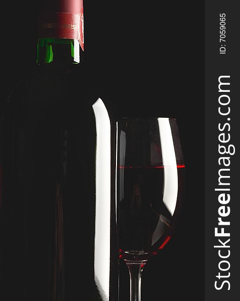Glass and bottle of red wine on black