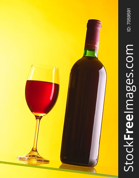 Glass and bottle of red wine on yellow background