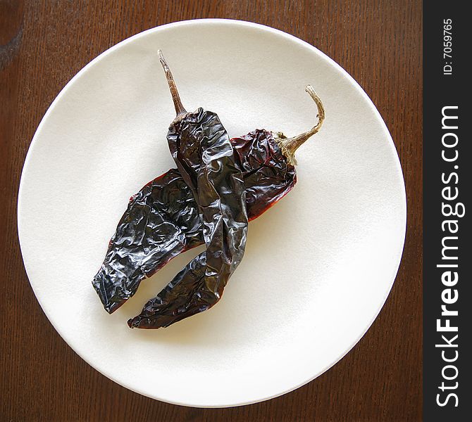 Two dried chili peppers on a white plate on a wood table. Two dried chili peppers on a white plate on a wood table