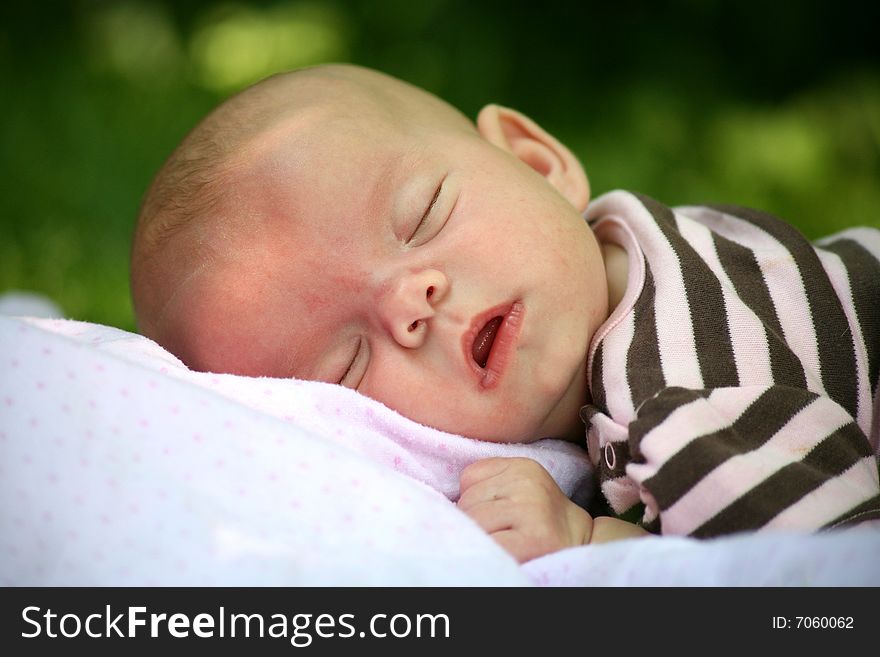 A peaceful, sleeping baby girl naps on a blanket on a summer's day outdoors. A peaceful, sleeping baby girl naps on a blanket on a summer's day outdoors.