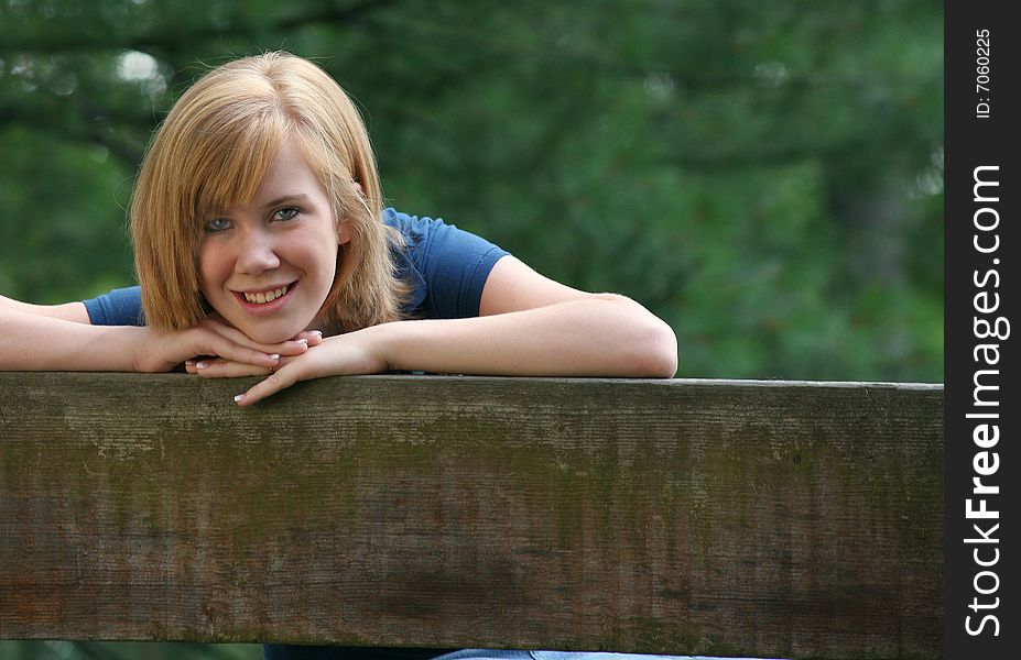 Teenage girl leaning on the back of a bench smiling with space on right and bottom for copy. Teenage girl leaning on the back of a bench smiling with space on right and bottom for copy.