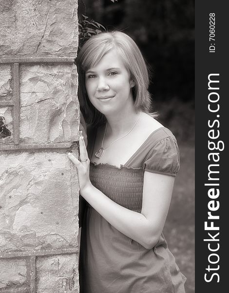 A teenage girl leans against a large outdoor fireplace in a simple black and white image. A teenage girl leans against a large outdoor fireplace in a simple black and white image.