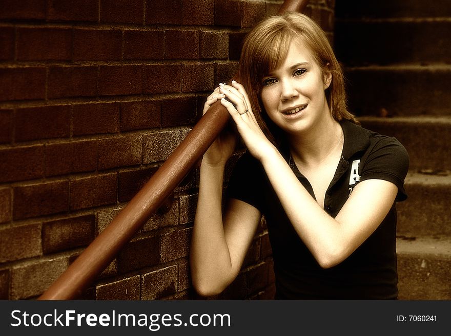 A teenage girl sits on a stairway near a brick building in a high contrast sepia image with a slight grain for an edgy, grungy look. Space for copy. A teenage girl sits on a stairway near a brick building in a high contrast sepia image with a slight grain for an edgy, grungy look. Space for copy.