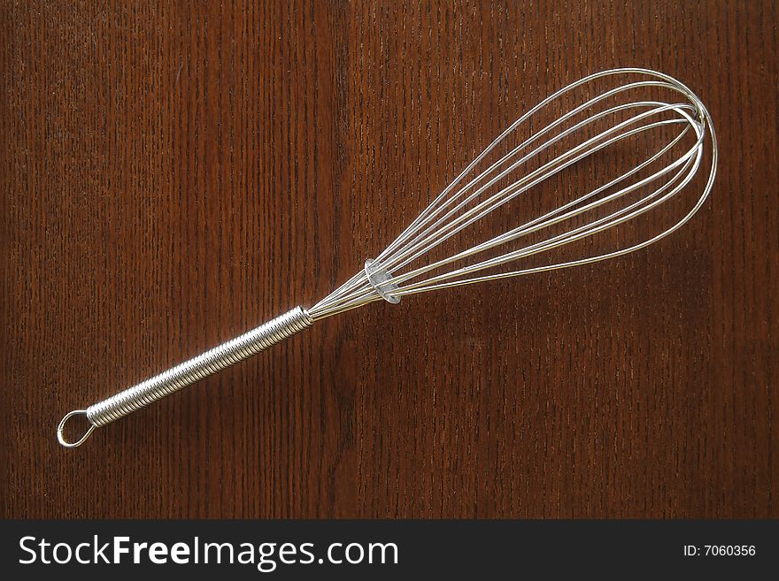 A stainless steel whisk on a wood background