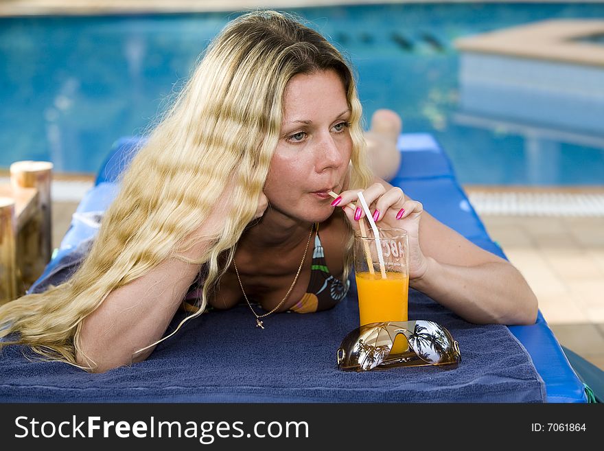 Beautiful blond woman drinking juice near swimming pool