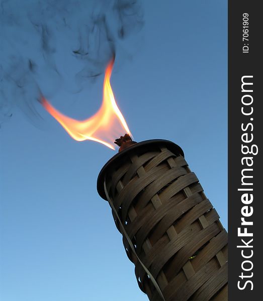 Bamboo Wicker Torch Ignited with Flames blazing against blue twilight sky