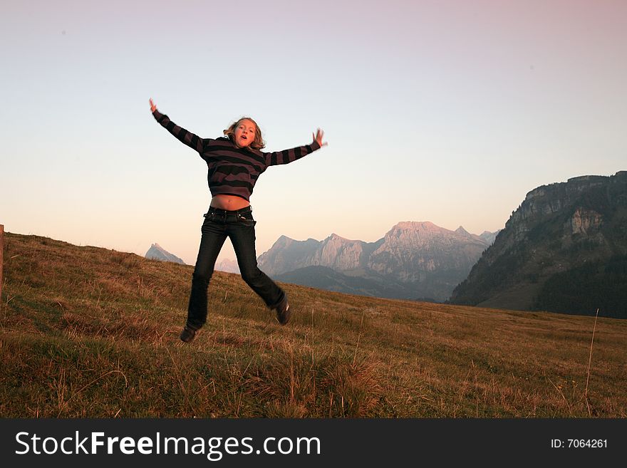 View of Swiss Alps with girl jumping in the evenings sunbeams. View of Swiss Alps with girl jumping in the evenings sunbeams