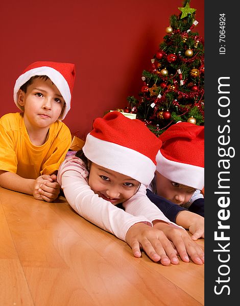 Little children as Santa in red cap laying on the floor with Christmas tree