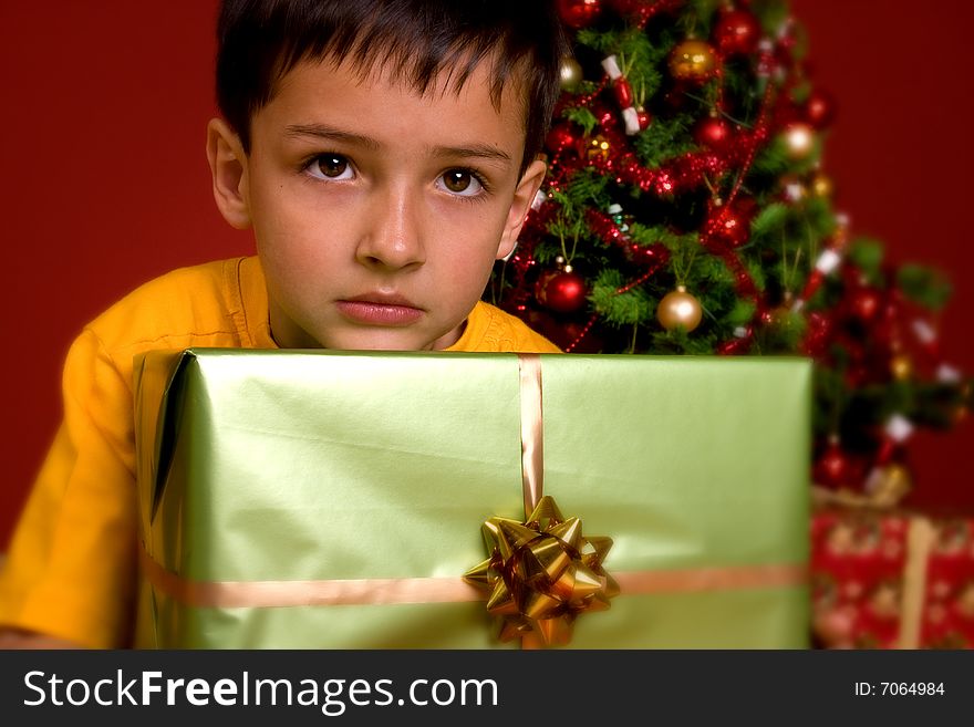 Boy carrying green gift in front of a Christmas Tree. Boy carrying green gift in front of a Christmas Tree.