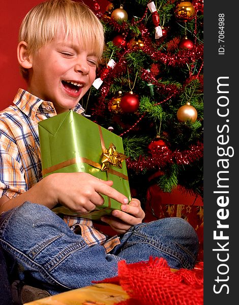 Laughing boy carrying green gift in front of a Christmas Tree. Laughing boy carrying green gift in front of a Christmas Tree.