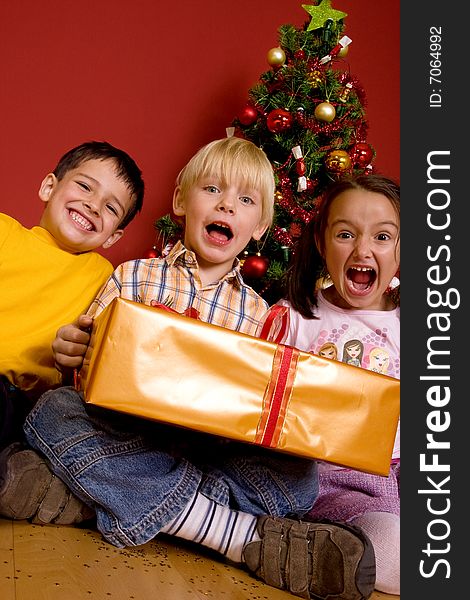Laughing children carrying gift in front of a Christmas Tree. Laughing children carrying gift in front of a Christmas Tree.