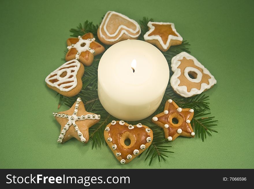 White pillar candle on fir branches surrounded by decorated gingerbread cookies on green background. White pillar candle on fir branches surrounded by decorated gingerbread cookies on green background