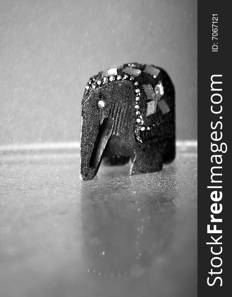 A photograph of a wooden elephant placed on glass table while sprinkled. A photograph of a wooden elephant placed on glass table while sprinkled.