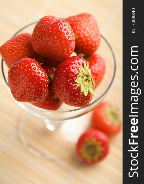 Ripe strawberries in glass bowl over bamboo mat