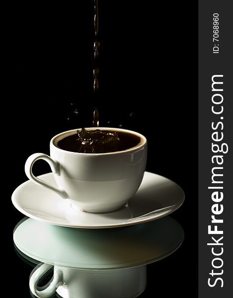 Coffee splashing into white cup over black background