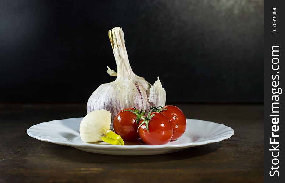 Tomatoes and clove of garlic in white plate. Tomatoes and clove of garlic in white plate