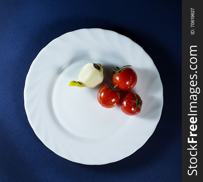 Tomatoes and clove of garlic in white plate on a dark blue background. Tomatoes and clove of garlic in white plate on a dark blue background