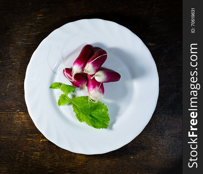 Fresh radishes in white plate on old wooden table