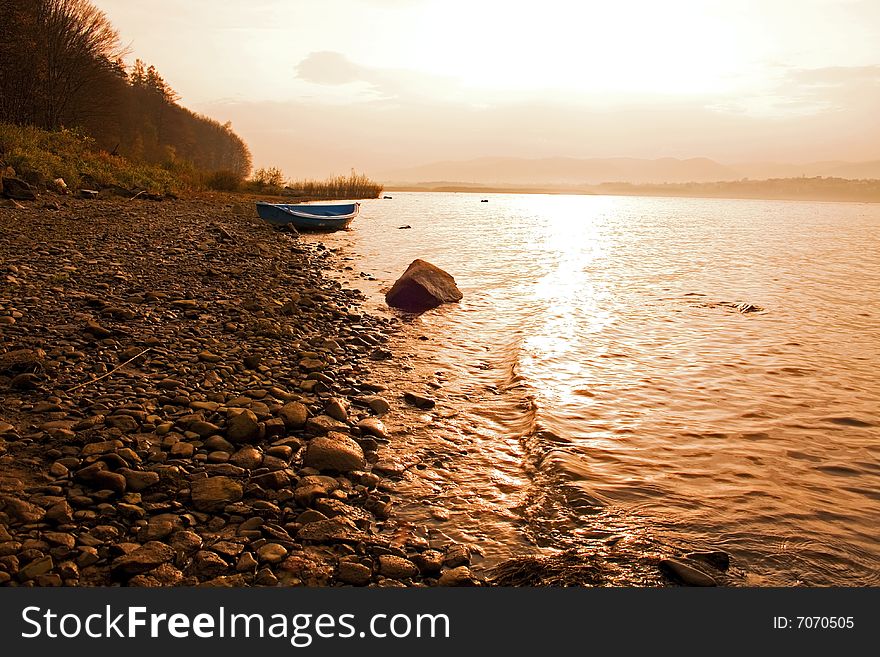 Blue boat on the lake shore and beautiful sunset view