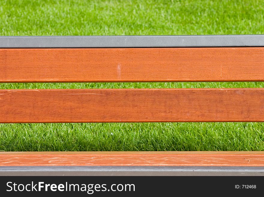 Horizontal close-up on nice wooden bench with bright green grass in background out of focus. Horizontal close-up on nice wooden bench with bright green grass in background out of focus