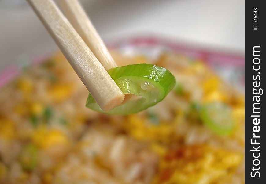 Extreme close-up of two chopsticks with pepper and a blurred plate with rice in the background