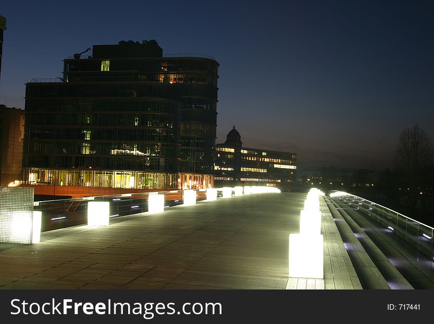 Modern pedestrian bridge in a city business district illuminated at the late evening