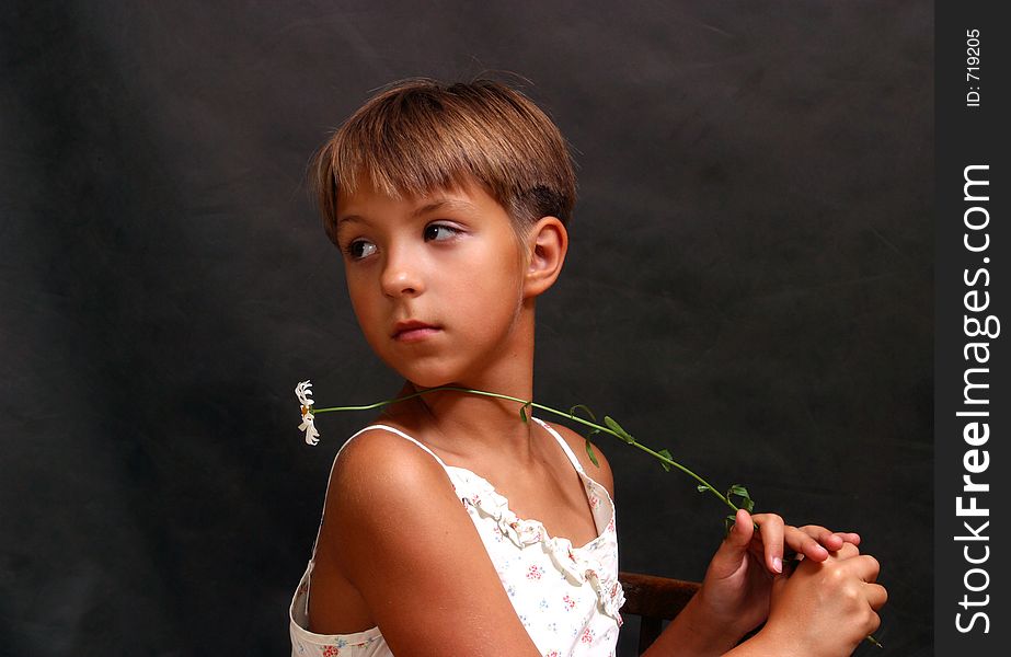 The girl looking to the left with a camomile on a dark background. The girl looking to the left with a camomile on a dark background.