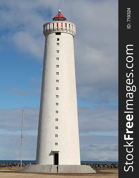 A big white lighthouse by the shore of the ocean