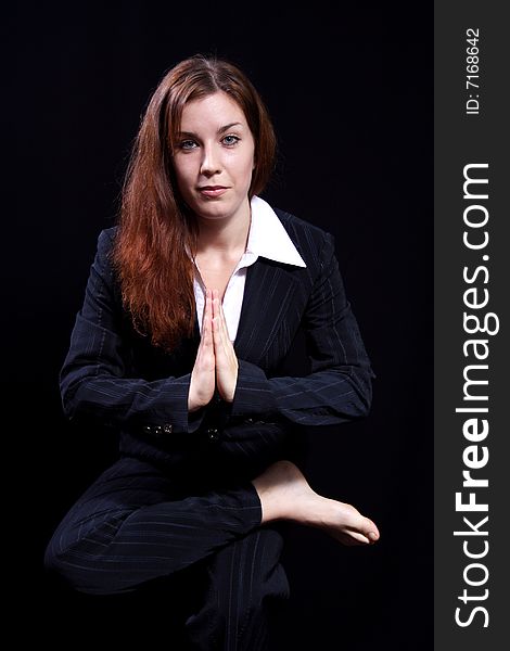 Girl in a business suit costs in one of poses of yoga on a black background. Girl in a business suit costs in one of poses of yoga on a black background