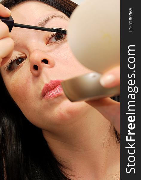 Young woman looking in the mirror and applying mascara. Young woman looking in the mirror and applying mascara