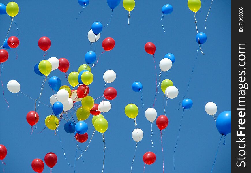 Bright balloons on streamers are floating off into a bright blue sky. Bright balloons on streamers are floating off into a bright blue sky.