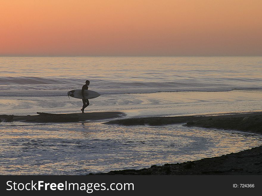 Surfer leaving ocean at twilight after a day of surfing. Surfer leaving ocean at twilight after a day of surfing.