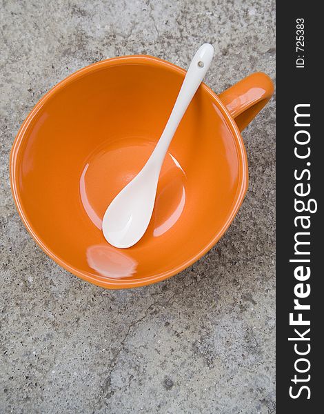 Orange cup with white spoon on a concrete table. Orange cup with white spoon on a concrete table