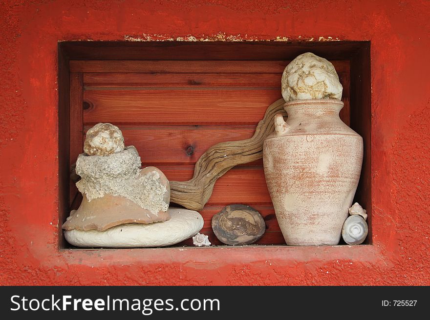 House detail with red closed window on a red wall background with a composition consisting stones , jug and cockle-shells