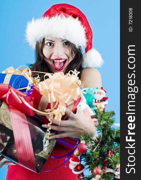 Half body portrait of smiling pretty teenage girl holding Christmas presents and wearing Santa hat, blue background. Half body portrait of smiling pretty teenage girl holding Christmas presents and wearing Santa hat, blue background.