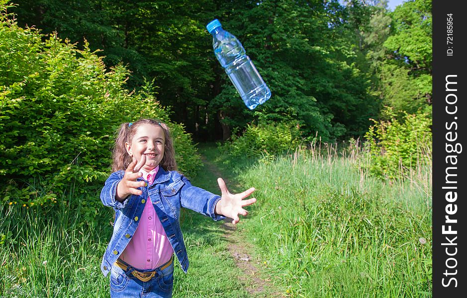 Girl in a blue denim jacket, catching a plastic bottle with water outside. Girl in a blue denim jacket, catching a plastic bottle with water outside