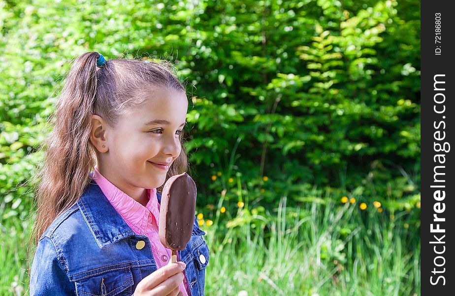 Smiling girl in a blue denim jacket eating ice cream outside. Smiling girl in a blue denim jacket eating ice cream outside