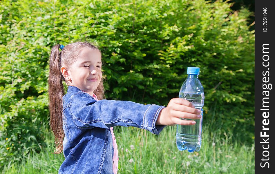 Girl in a blue denim jacket giving a plastic bottle with water. Girl in a blue denim jacket giving a plastic bottle with water