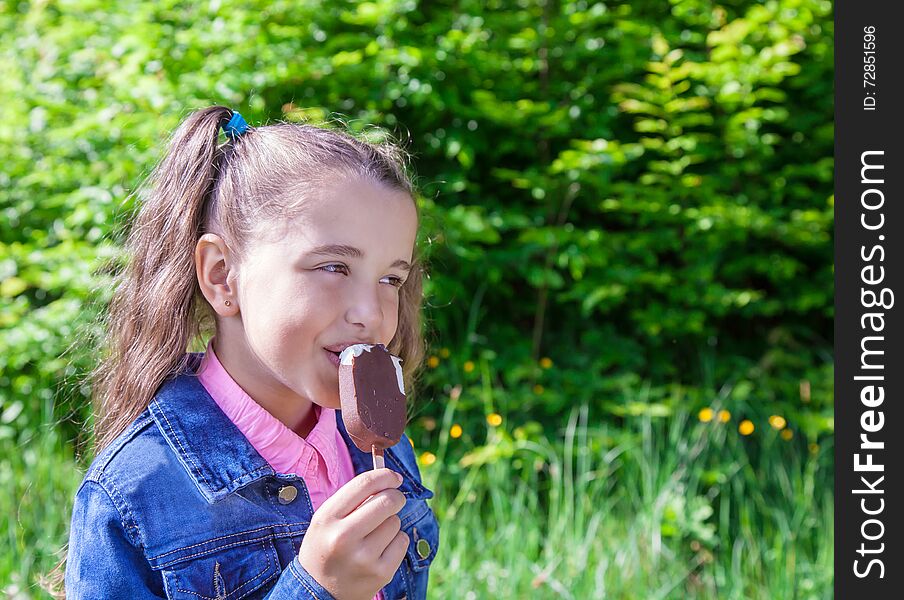 Girl in a blue denim jacket eating ice cream outside. Girl in a blue denim jacket eating ice cream outside