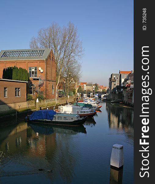 Row of boats with cabins sitting in a quiet canal surrounded by buildings. Row of boats with cabins sitting in a quiet canal surrounded by buildings