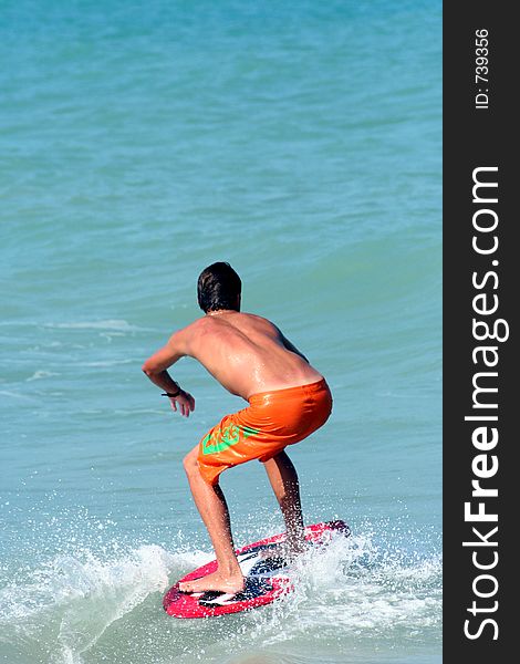 A brown haired teen boy surfs the shore at the ocean. A brown haired teen boy surfs the shore at the ocean