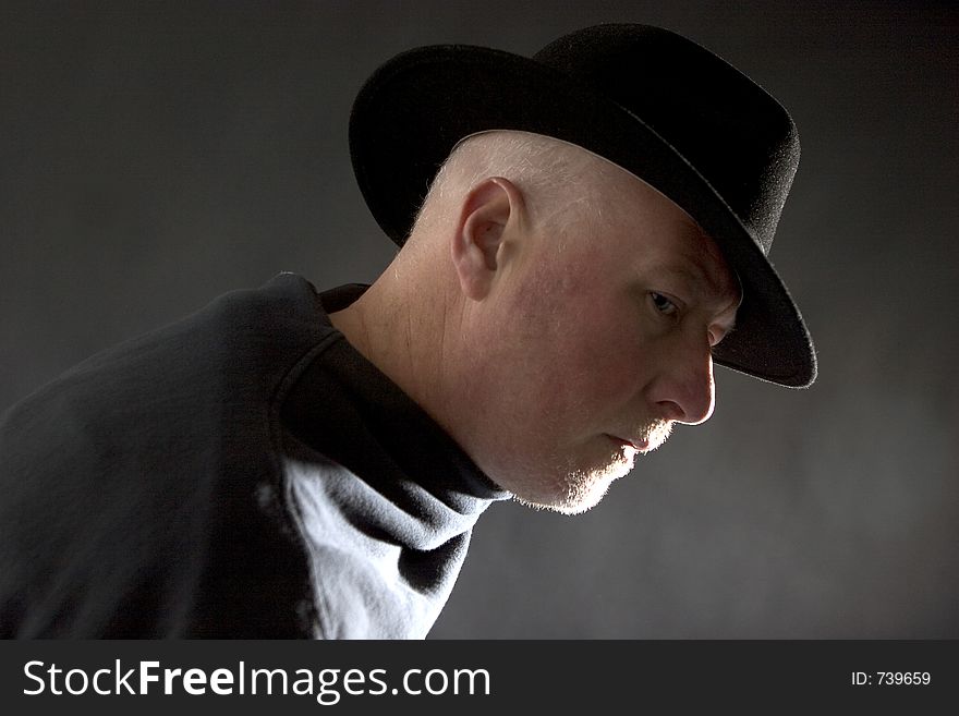 Middle aged man in profile, dark background and dark clothing and hat. Middle aged man in profile, dark background and dark clothing and hat