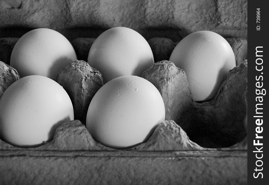 Five eggs in soft, dim light in a grey carton, arranged as to imply that an egg at the corner has been removed. Grescale image.