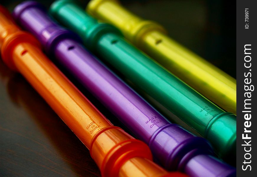 Colorful plastic musical instruments in shallow and soft focus, in orange, purple, green, and yellow on a deep brown background.